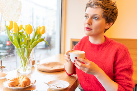 Mittlere erwachsene Frau mit kurzen blonden Haaren schaut durch das Fenster eines Cafés, lizenzfreies Stockfoto