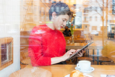 Mittlere erwachsene Frau in einem Café, die ein digitales Tablet mit Touchscreen benutzt, Blick aus dem Fenster - CUF51268