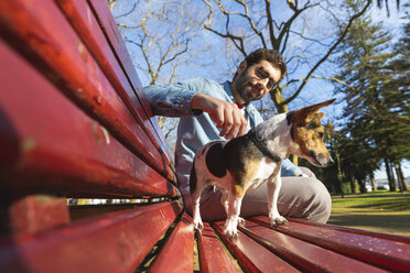 Junger Mann sitzt auf einer Parkbank und streichelt seinen Hund - WPEF01515