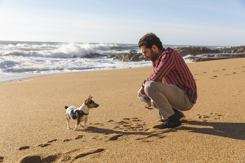 Portugal, Porto, junger Mann spielt am Strand mit seinem Hund, lizenzfreies Stockfoto