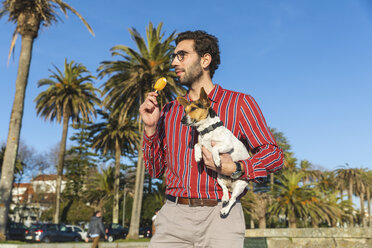 Junger Mann mit Hund auf dem Arm isst Eislutscher - WPEF01535
