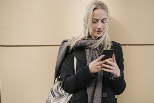 Junge Frau benutzt Handy an einer Wand - AHSF00363