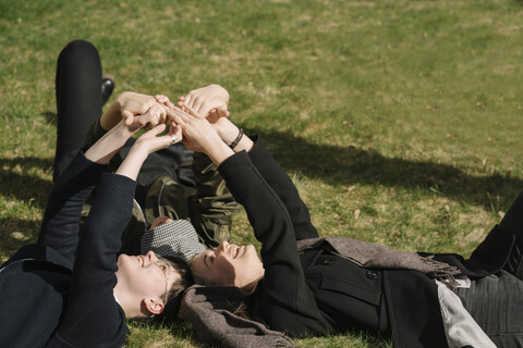 Gruppe junger Frauen, die im Gras liegen und ihre Hände zusammenlegen, lizenzfreies Stockfoto