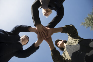 Worm's eye view of three women stacking their hands under blue sky - AHSF00398