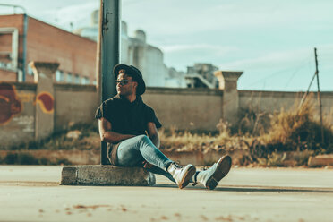 Young man sitting on the floor with a hat, looking sideways - OCAF00374