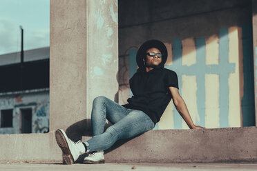 Young man sitting on ground with a hat, looking sideways - OCAF00377