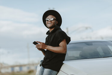 Porträt eines jungen Mannes, der mit dem Telefon eine E-Mail verschickt, lachend - OCAF00379