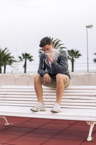 Junger Mann raucht einen Joint mit Palmen im Hintergrund, lizenzfreies Stockfoto