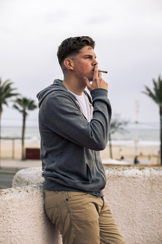 Young man smoking a joint with palm trees in the background stock photo