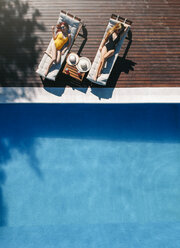 Two beautiful women sunbathing on a terrace next to the pool - OCMF00453