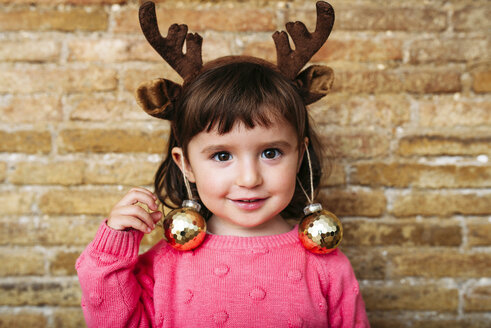 Portrait of smiling toddler girl wearing reindeer antlers headband and Christmas baubles - GEMF02942