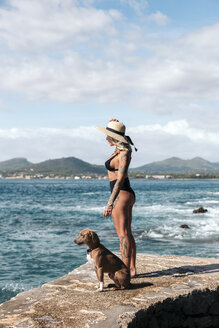 Spanien, Mallorca, tätowierte Frau steht neben ihrem Hund und schaut auf das Meer - LOTF00069