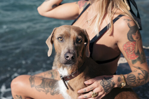 Spain, Mallorca, portrait of dog sitting besides tattooed woman in front of the sea - LOTF00070