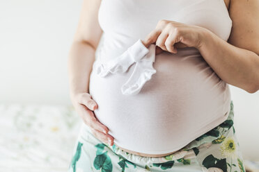 Mittelteil einer schwangeren Frau, die die Socken ihres Babys hält - FLMF00202