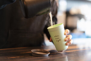 Mann gießt heiße Milch in eine Tasse für Coffee to go, Nahaufnahme - DIGF07031