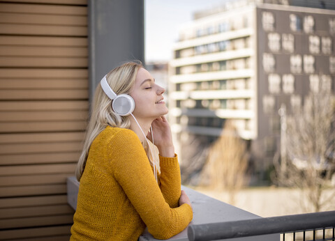 Lächelnde junge Frau mit geschlossenen Augen, die mit Kopfhörern Musik hört, lizenzfreies Stockfoto