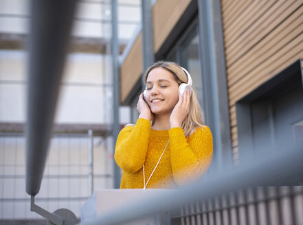 Porträt einer lächelnden jungen Frau, die mit Kopfhörern Musik hört - BFRF02011