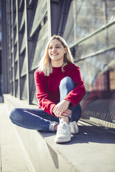 Porträt einer lächelnden jungen Frau, die im Sonnenlicht an der Wand sitzt - BFRF02017