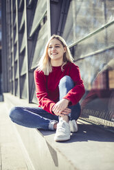 Portrait of smiling young woman sitting on wall at sunlight - BFRF02017