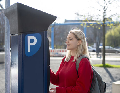 Smiling young woman using pay and display machine - BFRF02022