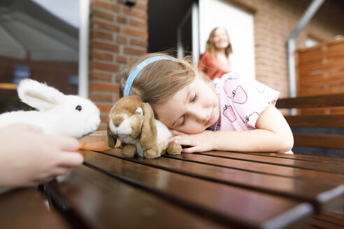 Mädchen auf Gartentisch liegend mit Spielzeughäschen - KMKF00950