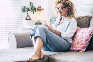 Woman on couch at home with coffee mug and cell phone - SIPF01953