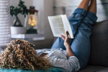 Woman lying on couch at home reading a book - SIPF01955