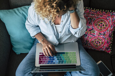 Frau benutzt Laptop mit mehrfarbiger Tastatur auf der Couch zu Hause - SIPF01960