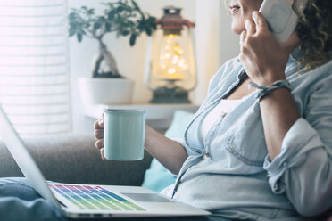 Nahaufnahme einer Frau auf der Couch zu Hause mit Kaffeetasse, Laptop und Mobiltelefon - SIPF01964