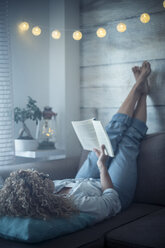 Woman lying on couch at home reading a book - SIPF01970