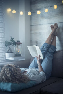 Frau liegt auf der Couch zu Hause und liest ein Buch - SIPF01970