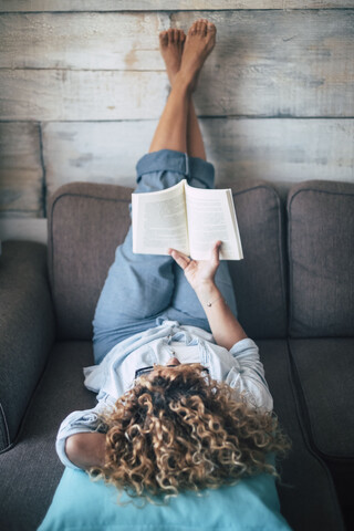 Frau liegt auf der Couch zu Hause und liest ein Buch, lizenzfreies Stockfoto