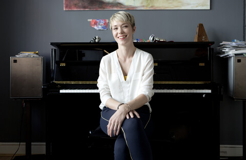 Portrait of laughing woman sitting in her music room in front of piano stock photo