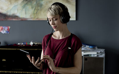 Porträt einer blonden Frau, die mit Kopfhörern und digitalem Tablet Musik hört - FLLF00133