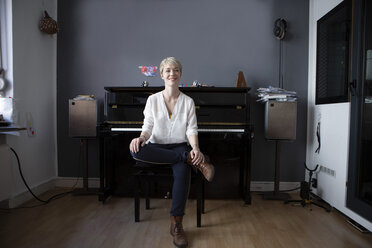 Portrait of relaxed woman sitting in her music room in front of piano - FLLF00134