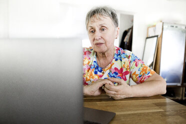 Ältere Frau sitzt zu Hause am Tisch und benutzt einen Laptop - KMKF00962