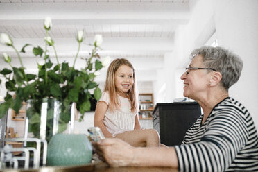 Happy grandmother with cell phone and granddaughter at home - KMKF00969