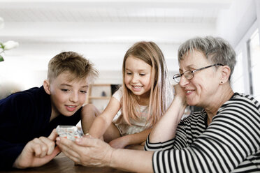 Happy grandmother and grandchildren using cell phone at home stock photo