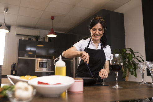 Lächelnde Frau beim Kochen in der Küche mit einer Pfanne - ABZF02346