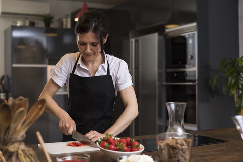 Frau schneidet Erdbeeren mit einem Messer in einer Küche, lizenzfreies Stockfoto