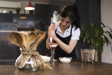 Frau schmiert Sahne auf ein Dessert in der Küche - ABZF02375