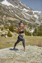 Junge Frau macht Yoga stehend auf einem Felsen in der Natur, Kriegerpose - JPF00397