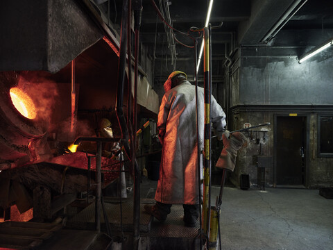 Industrie, Arbeiter am Schmelzofen beim Schmelzen von Kupfer, im Feuerschutzanzug, lizenzfreies Stockfoto