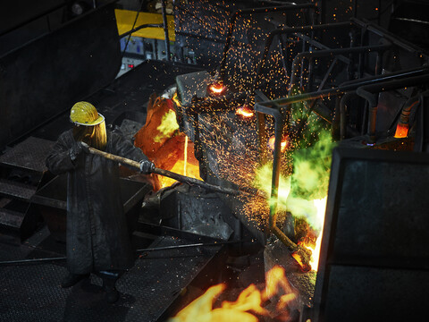 Industrie, Arbeiter am Schmelzofen beim Schmelzen von Kupfer, im Feuerschutzanzug, lizenzfreies Stockfoto