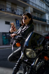 Portrait of young woman leaning against motorbike looking at smartphone - OCMF00457