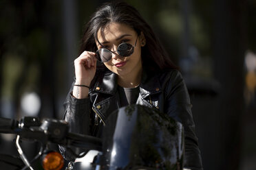 Porträt einer jungen Motorradfahrerin mit Sonnenbrille und schwarzer Lederjacke - OCMF00458
