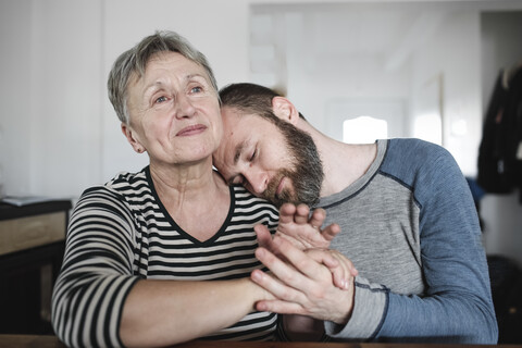 Affectionate adult son with senior mother at home stock photo