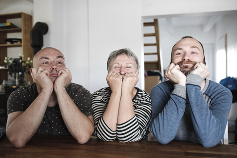 Portrait of adult sons with senior mother sitting at table at home with head in hands stock photo