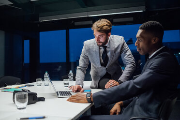 Geschäftsleute, die während einer Besprechung am Konferenztisch auf einen Laptop schauen - CUF51322