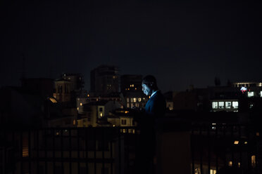 Young businessman using laptop on office balcony at night - CUF51338